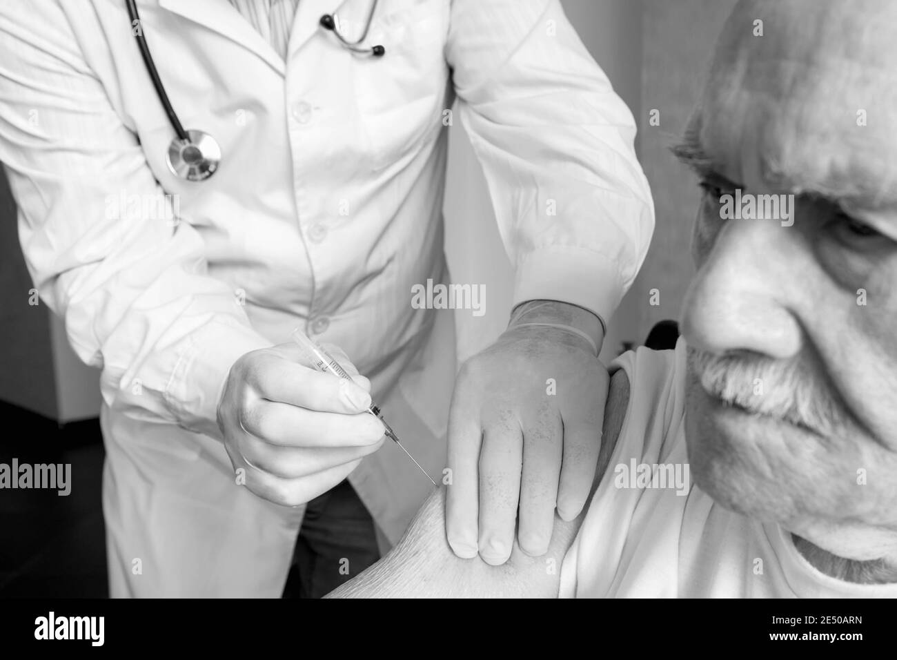 Vaccination of the elderly against viruses. A medical worker gives an injection of the covid-19 vaccine to an old, white-haired man. The old man looks Stock Photo