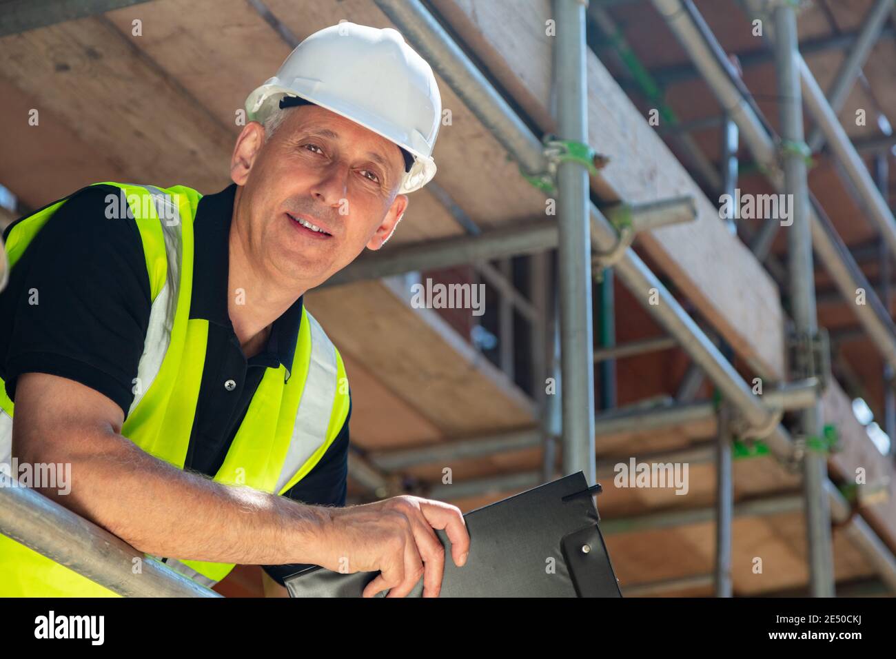 Male builder foreman, construction worker or site manager holding a clipboard, wearing a white hard hat and hi vis vest Stock Photo