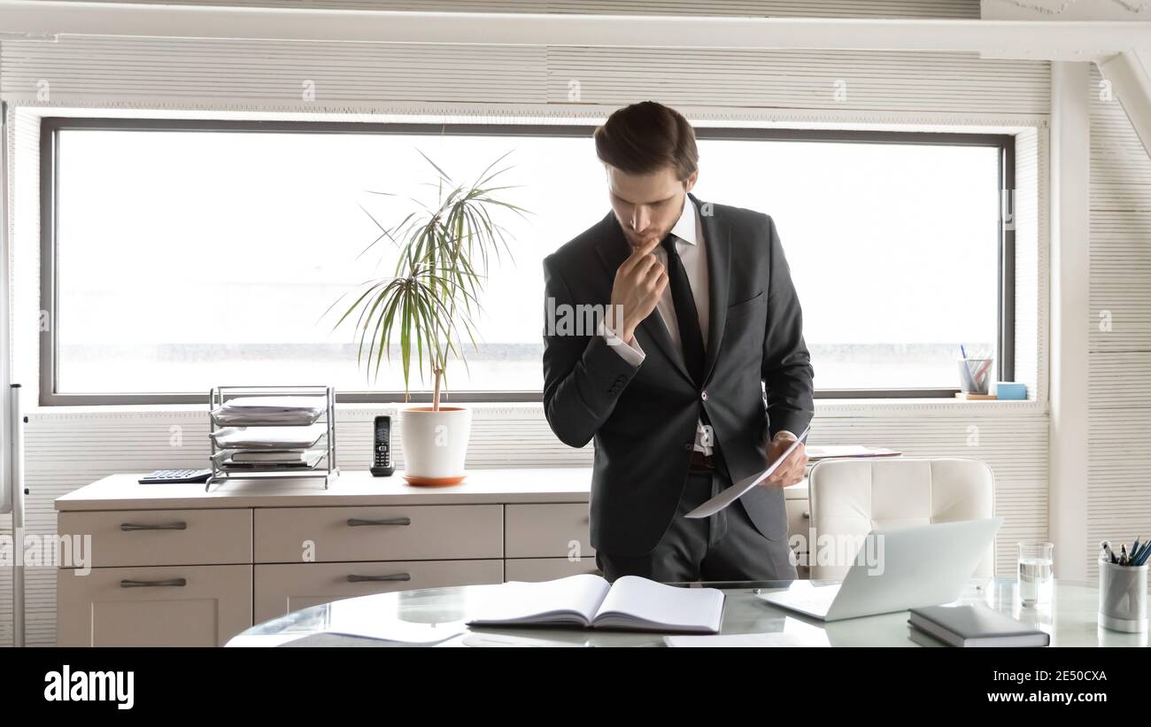 Thoughtful businessman touching chin, checking financial documents in office Stock Photo