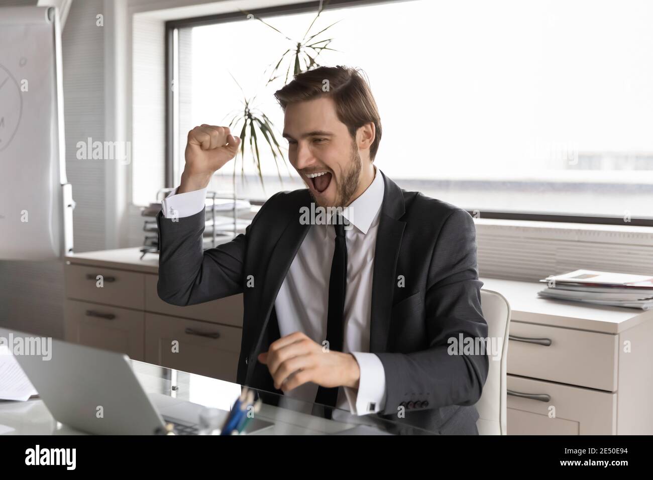 Overjoyed businessman wearing suit looking at laptop screen, reading news Stock Photo
