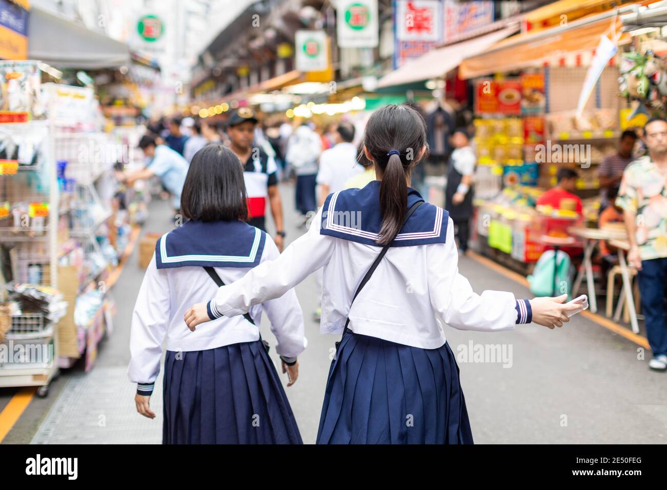 Close up of two young girls wearing the sailor walking away in a colorful Ameyoko market in Tokyo Stock Photo