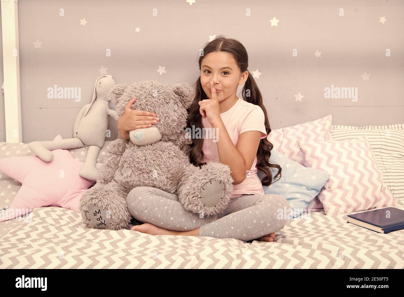 Girls secret. Cute kid show silence finger gesture. Little secret. Small girl play with teddy bear in bed. Keeping mouth shut. Being quiet. Silence and shushing. Top secret. Can you keep secret. Stock Photo