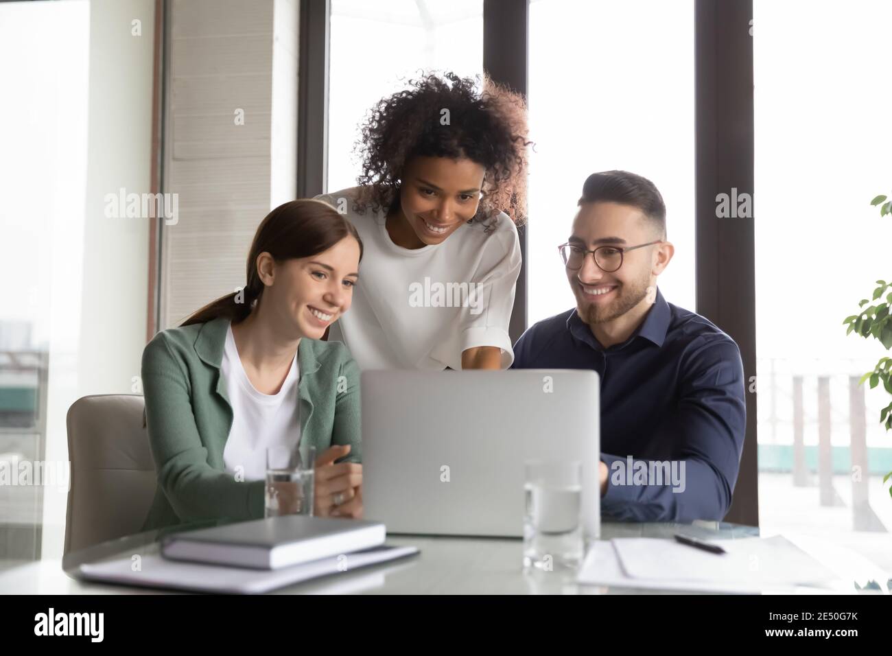 Three happy diverse colleagues working on project together, using laptop Stock Photo