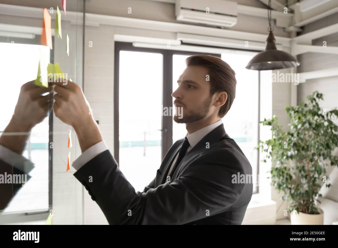 Close up thoughtful businessman adding sticky paper on board Stock Photo