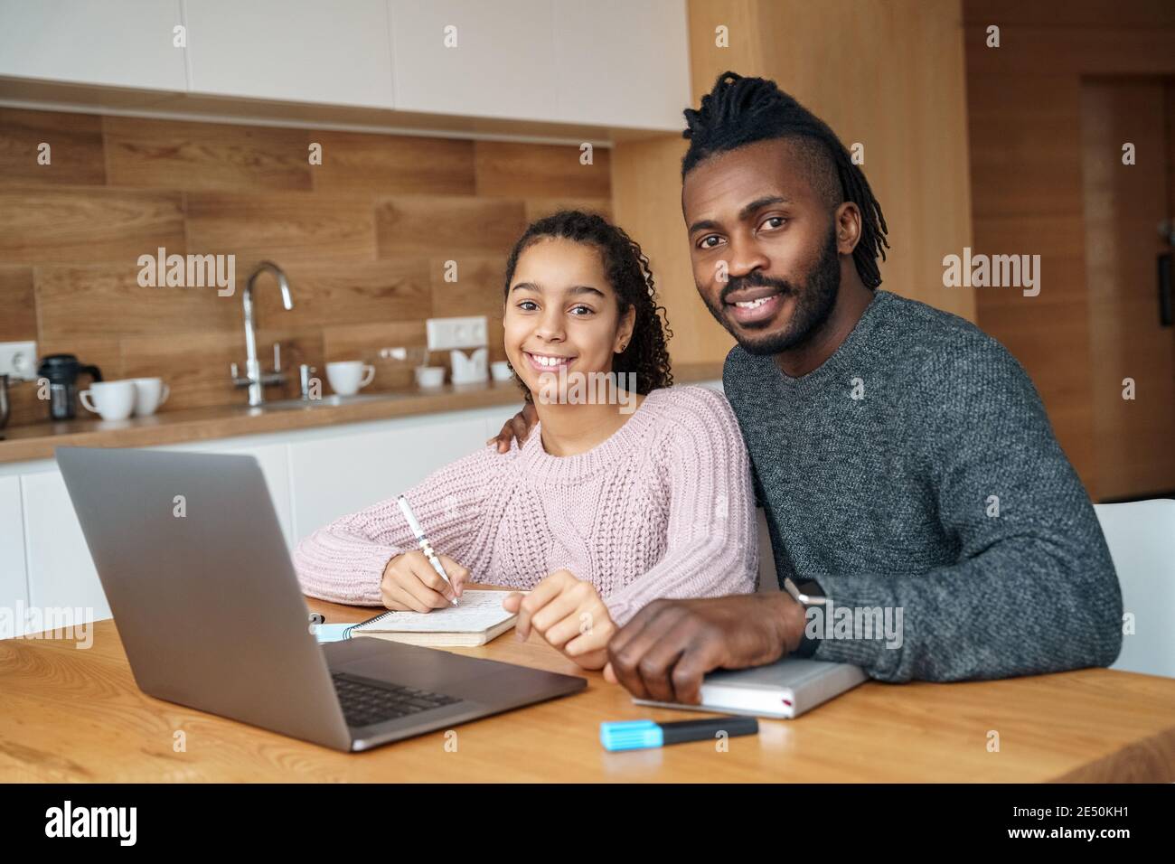 Happy African American father helps to study online to his teen age daughter. Stock Photo