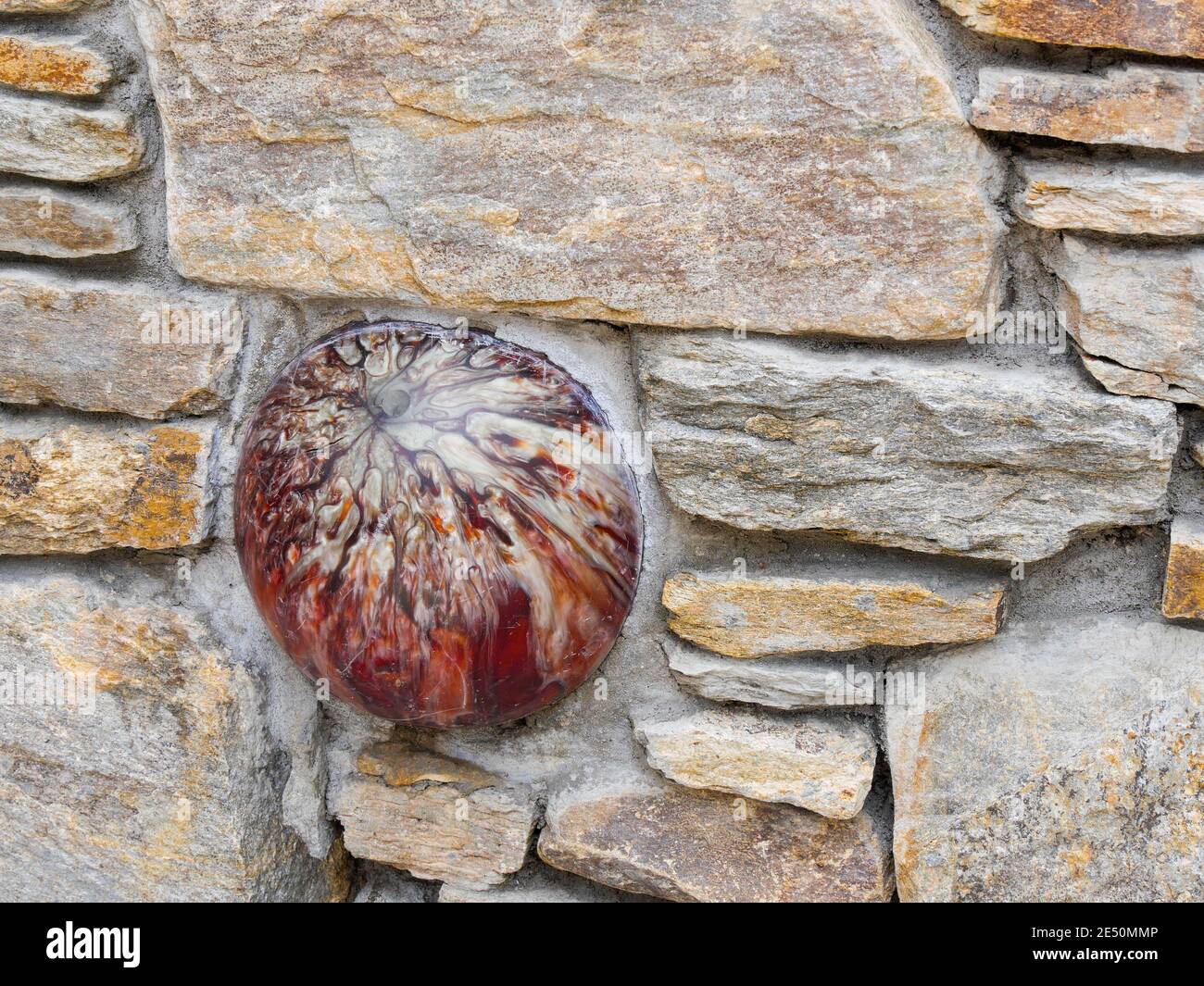 red marbleized bowling ball embedded in a stone wall for the concept of dare to be different or stand out in a crowd Stock Photo