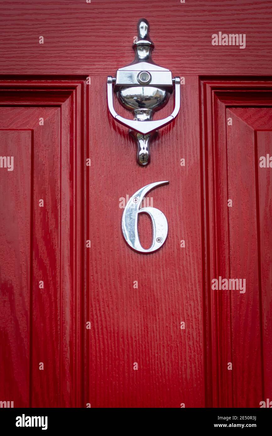 SIlver number 6 on a red wooden front dor with door knocker and peephole Stock Photo