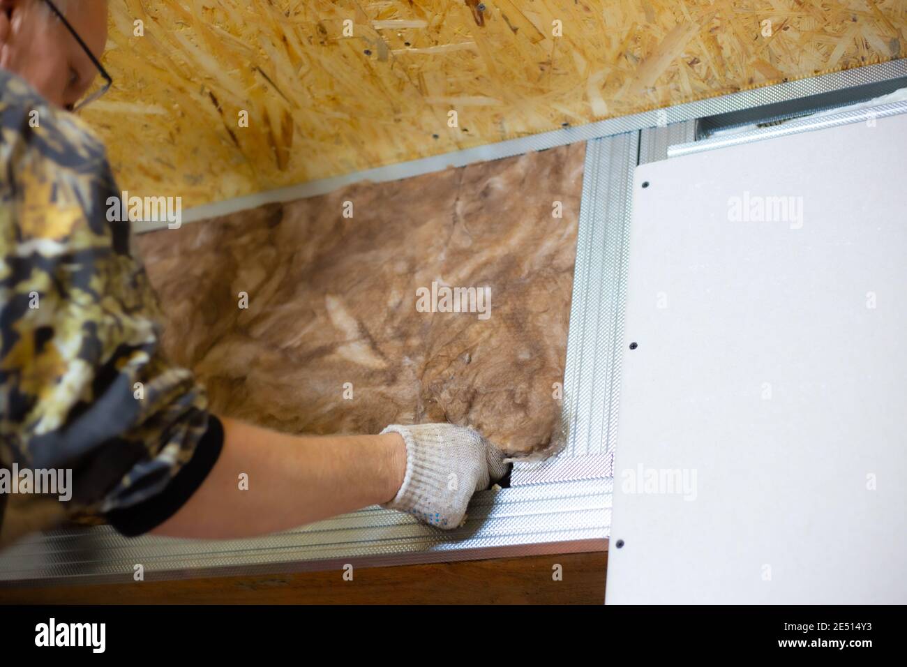 Insulation of the house with mineral wool. A man installs a block of heat-insulating material on the wall for further plasterboard cladding. Stock Photo