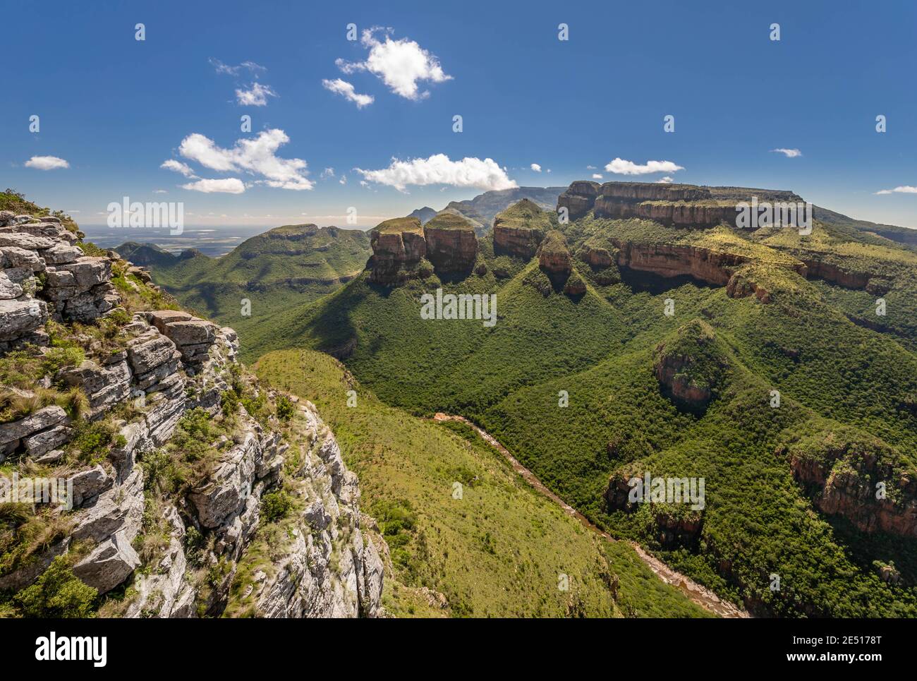 Wide angle shot of the Blyde River Canyon in South Africa as seen from a viewpoint, under a blue sky with puffy cloud Stock Photo