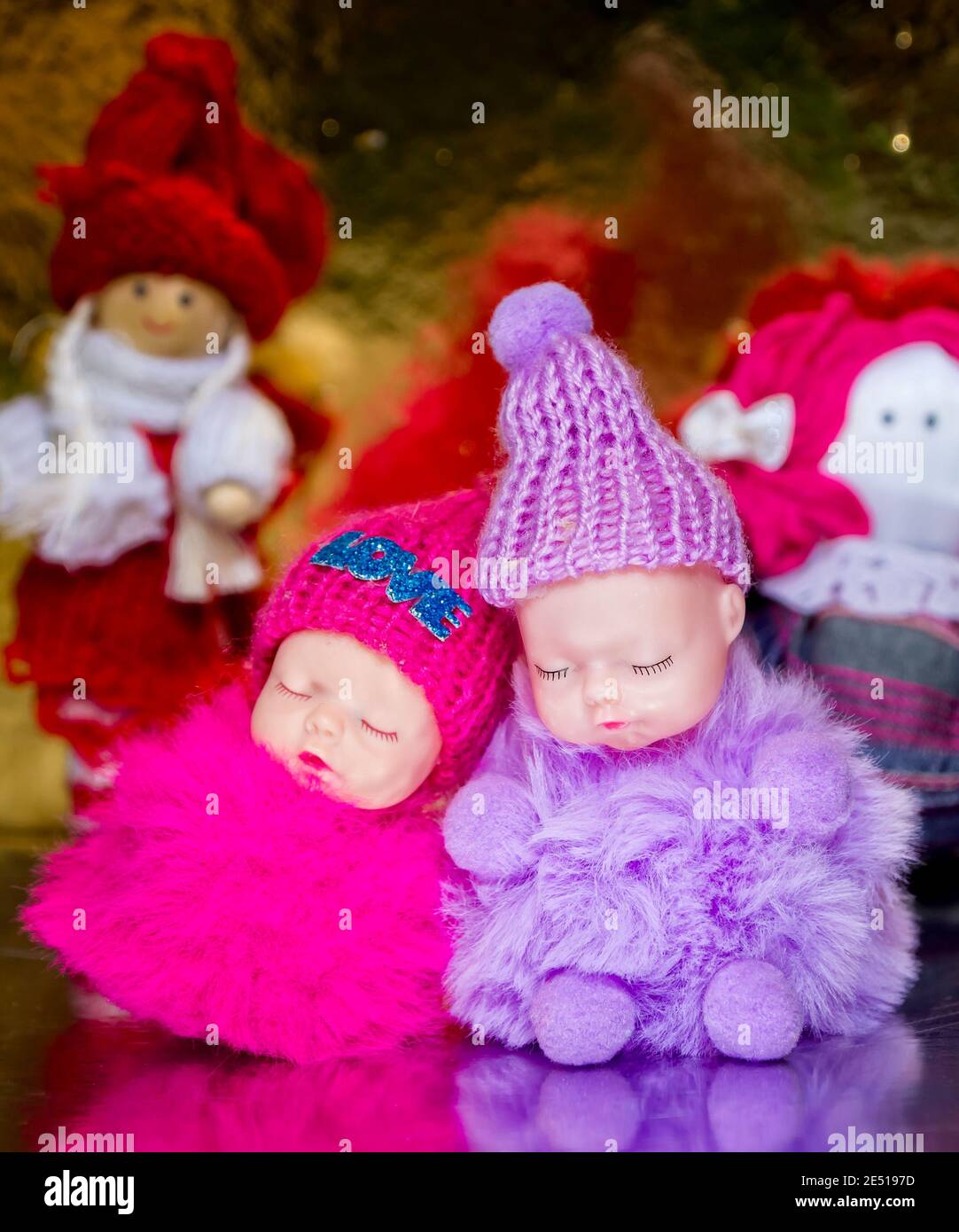 Two toy figures of small children in warm clothes Pink and red are sleeping. Love is written on the cap. And handmade toys for children's. Golden back Stock Photo