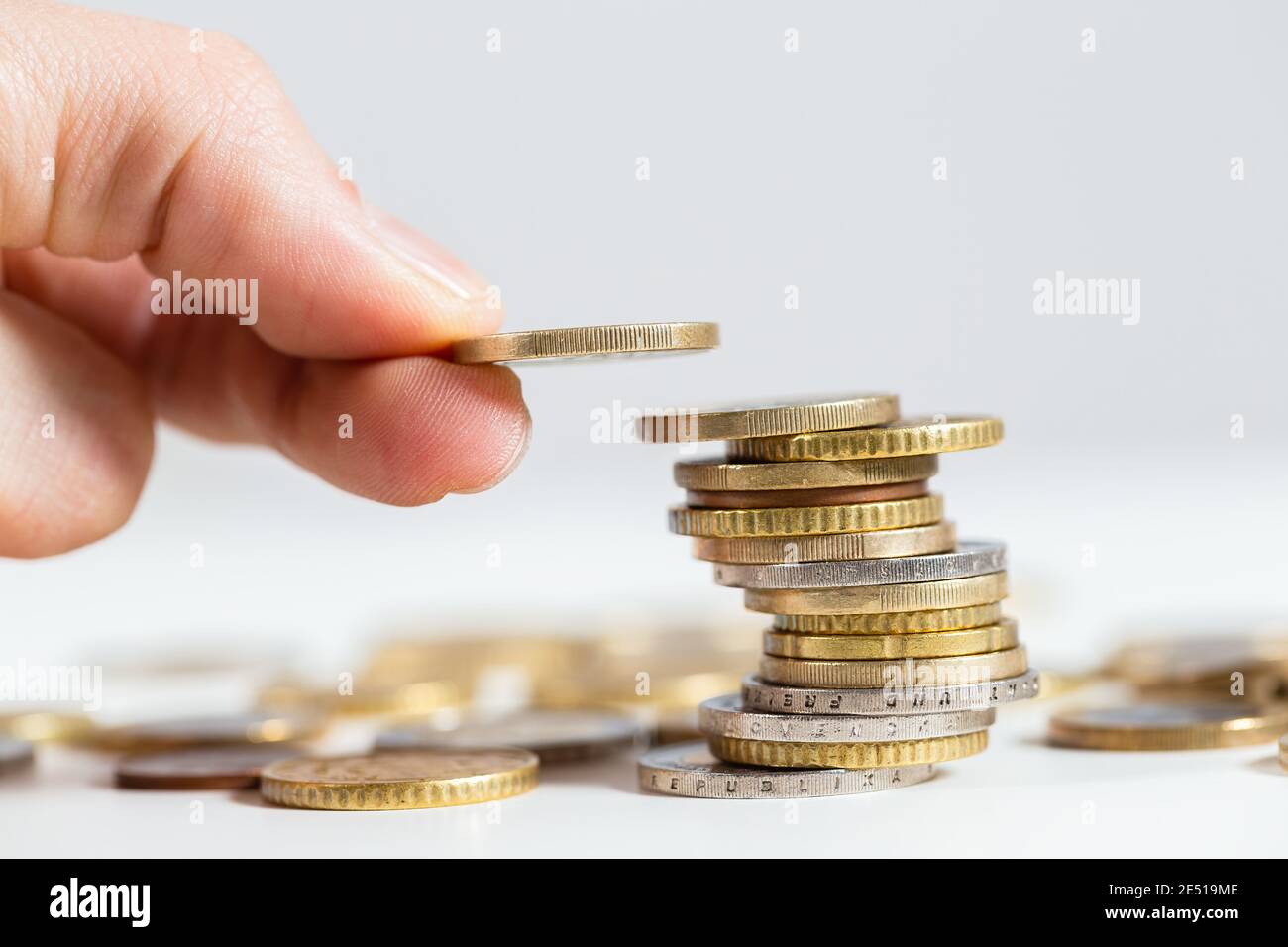Fingers holding coin over the stack of money from close up Stock Photo