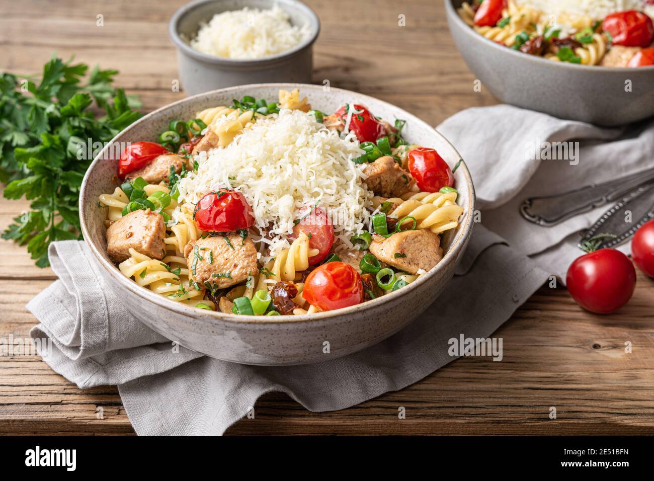 Chicken pasta salad with roasted and sun-dried tomatoes, topped with green onion slices and grated cheese on wooden background Stock Photo