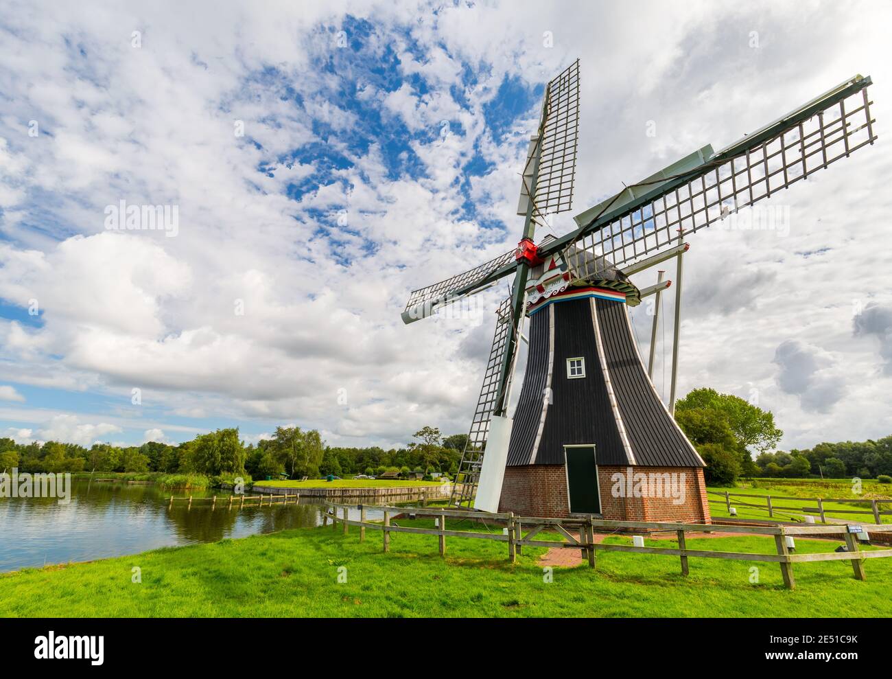 Wide angle view of a dutch landscape, with meadows, canals and an ancient black and white windmill in the foreground Stock Photo