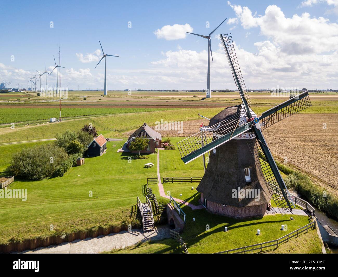 Aerial wide angle view of an ancient windmill against large wind farm of modern wind turbines Stock Photo
