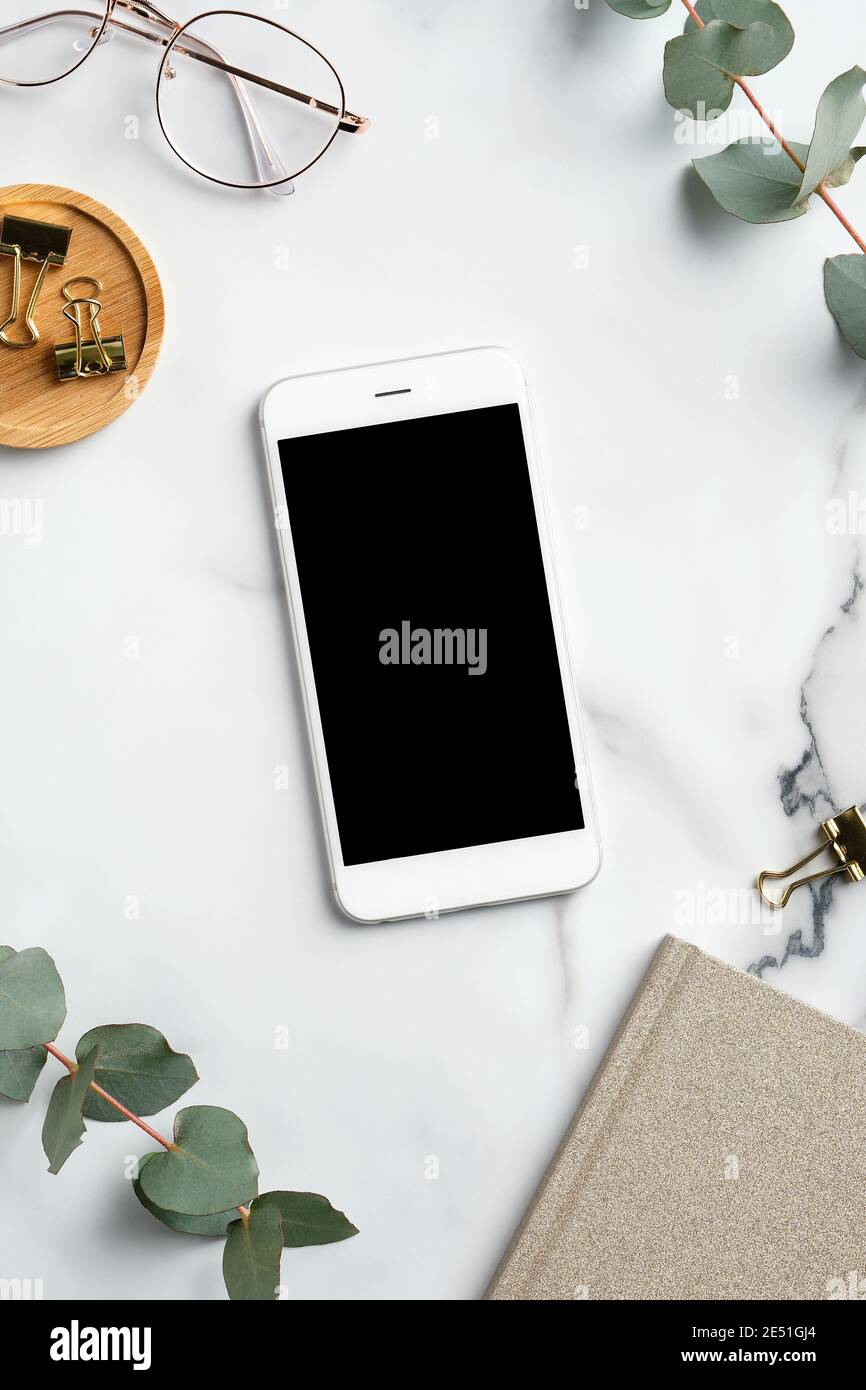 Home office workspace with smartphone mockup, feminine glasses, notebook, eucalyptus leaves. Flat lay, top view, copy space. Stock Photo