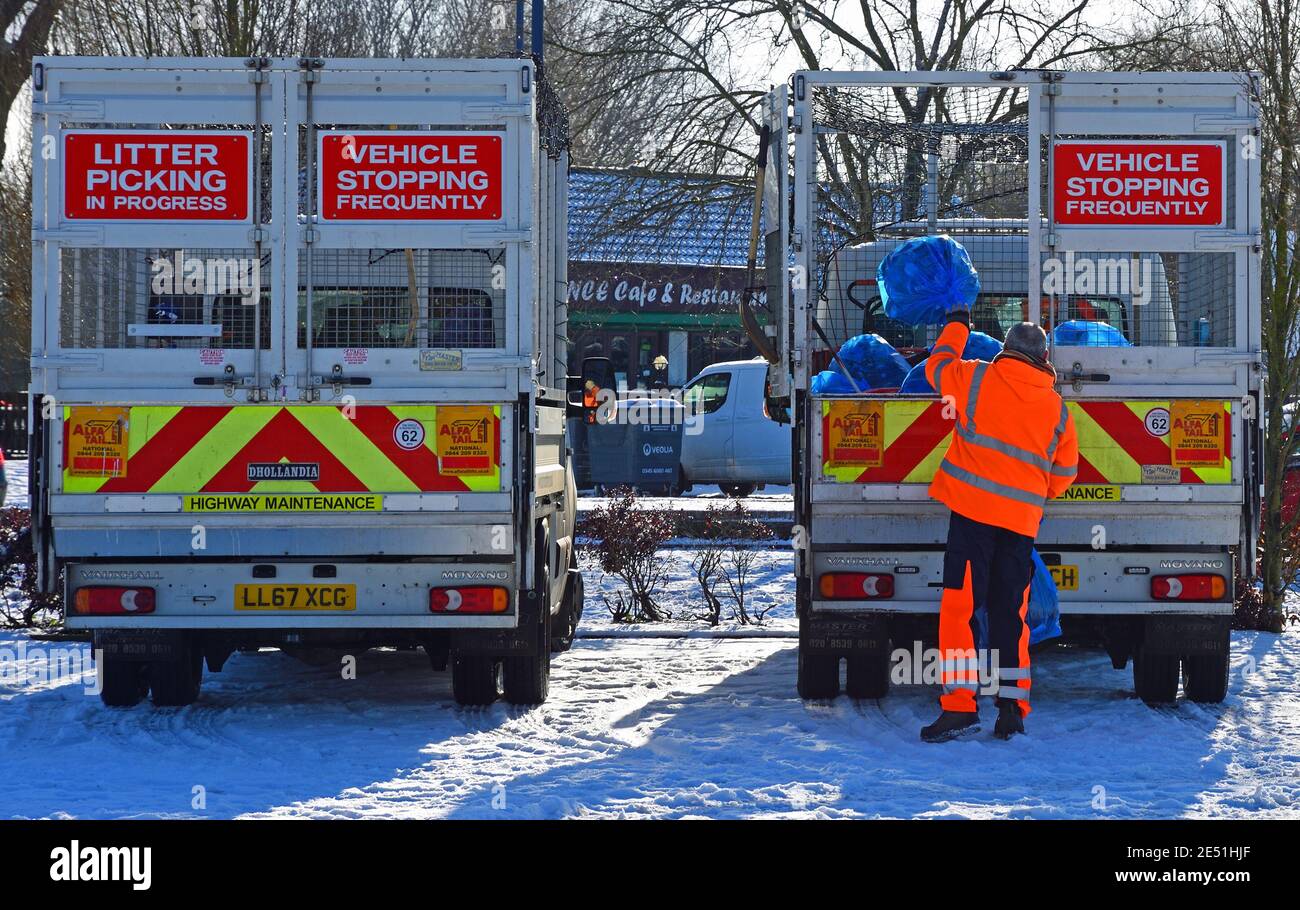 Two trucks collecting rubbish in the snow. Bin man throwing rubbish bag in the back of truck. Stock Photo