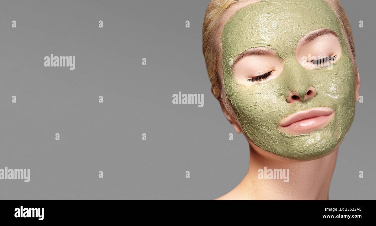 Beautiful Woman Applying Green Facial Mask. Beauty Treatments. Close-up Portrait of Spa Girl Apply Clay Facial mask on grey background Stock Photo
