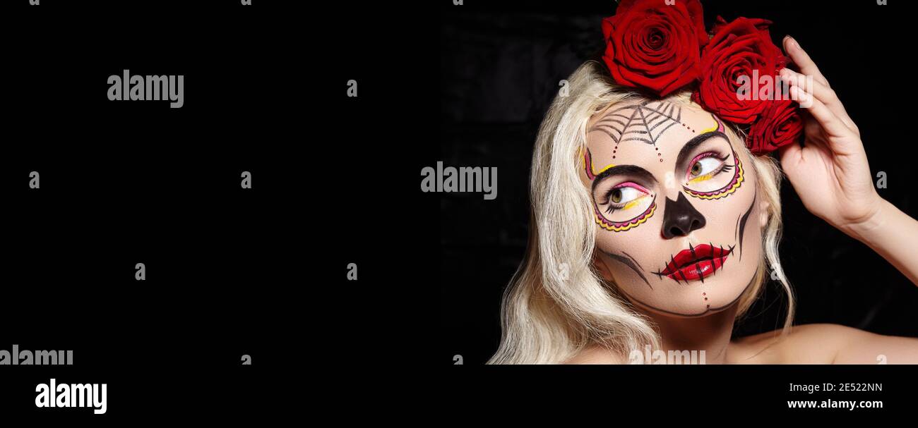 Beautiful Halloween Make-Up Style. Blond Model Wear Sugar Skull Makeup with Red Roses, pale Skin Tones and Waves Hair. Dia de los Muertos or Santa Mue Stock Photo