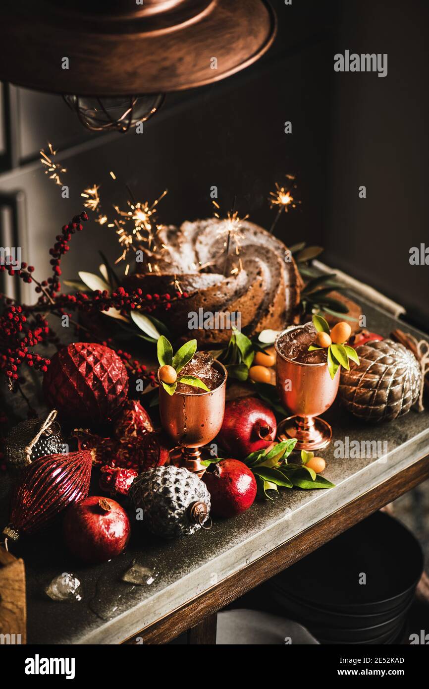 Christmas or Thanksgiving Day festive homemade bundt cake with sparklers and winter ice refreshing citrus cocktails in copper goblets on kitchen counter. Winter holidays festive mood concept Stock Photo