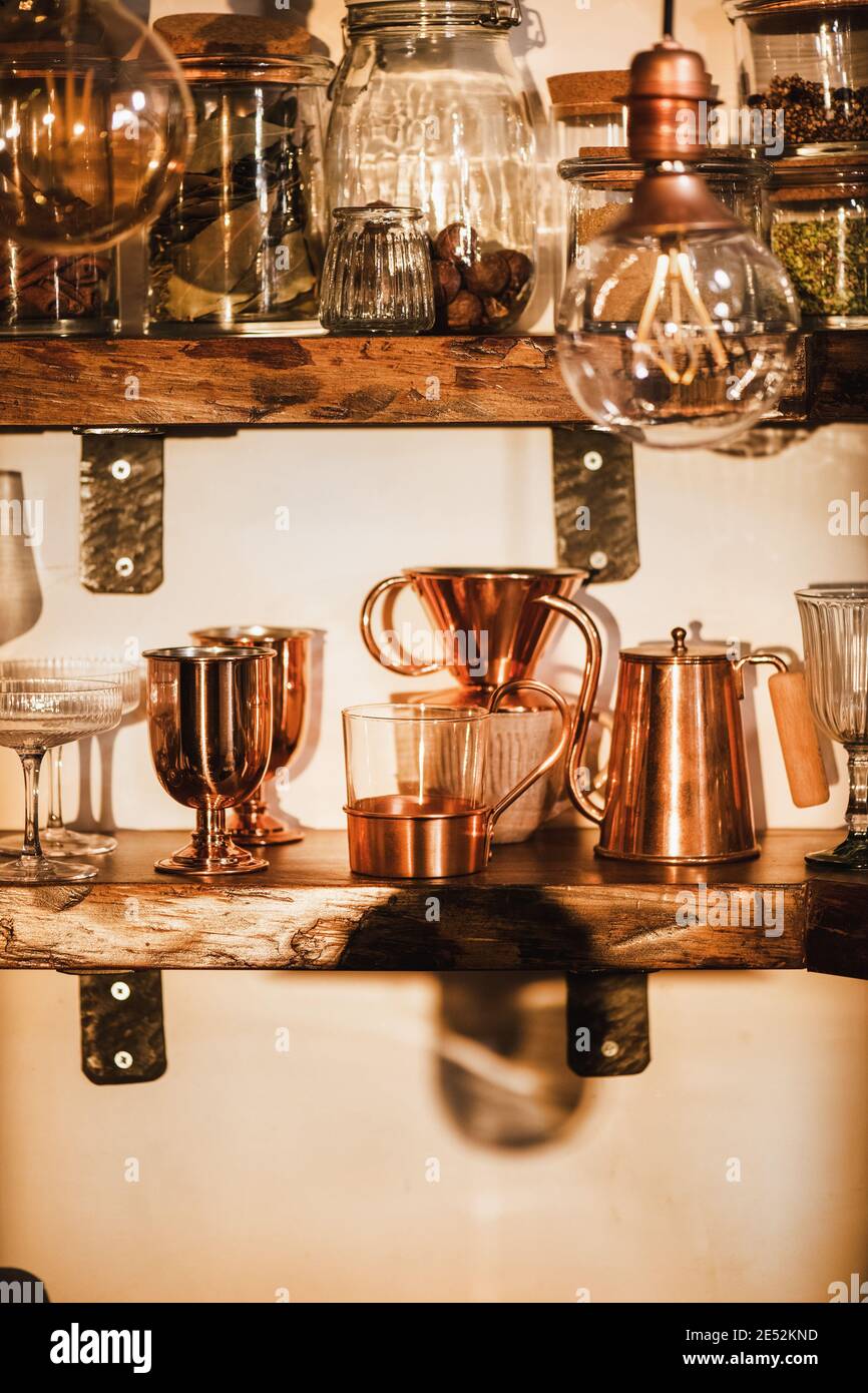Kitchen shelves with various glass and copper glassware, mugs, tumblers and coffee utencils in beautiful daylight. Interiors detail and lifestyle mood concept Stock Photo