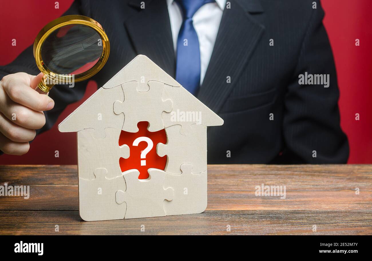 A man examines a house with a missing puzzle inside. Property valuation. Finding problems and structural hidden defects. Checking for compliance with Stock Photo