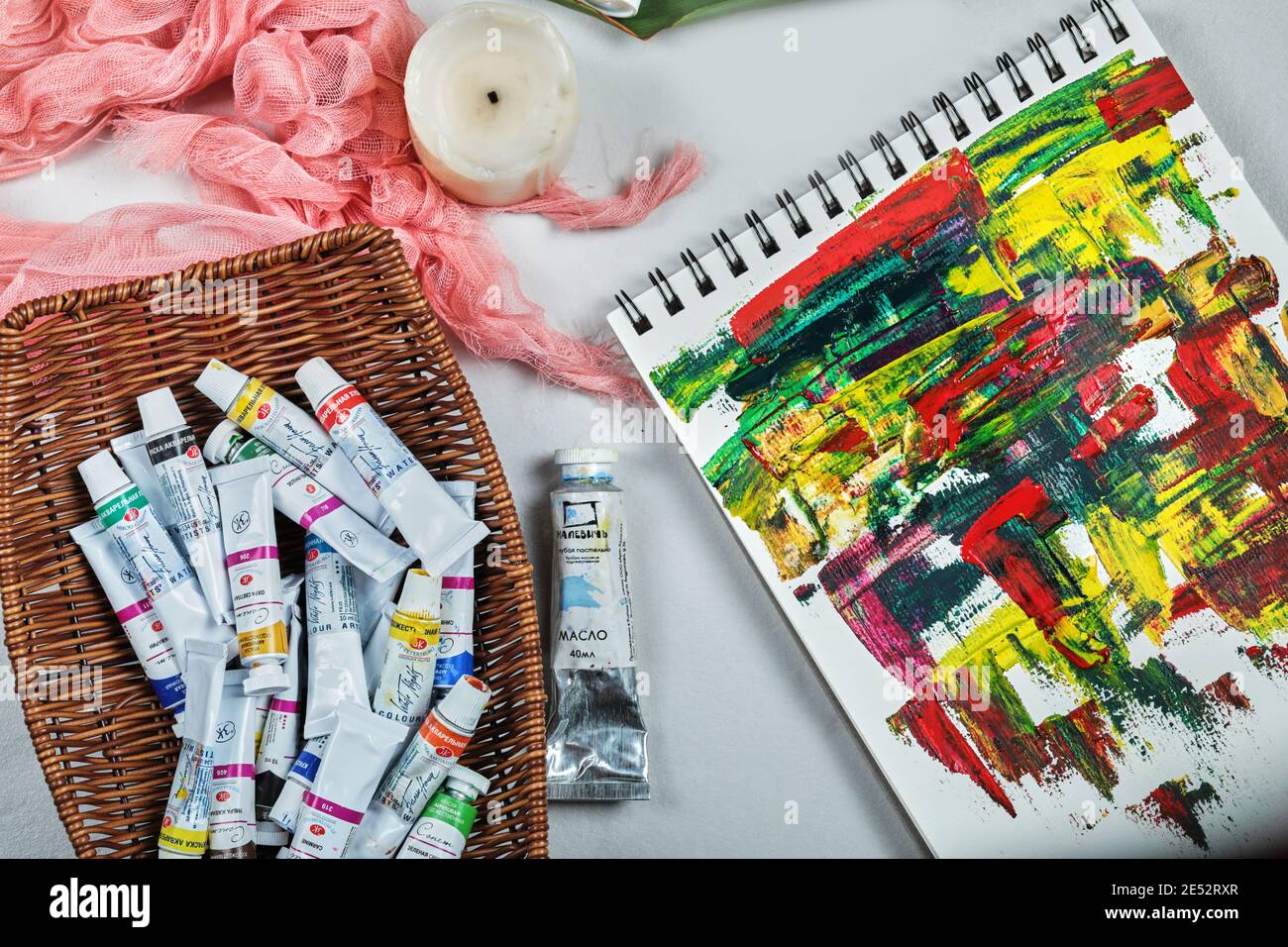 Art supplies. Bunch of paint tubes in wooden basket and abstract art on white background Stock Photo