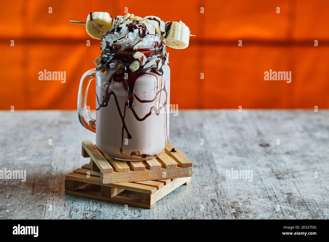 Chocolate smoothie with choco syrup, banana and whipped cream on the wooden board in the bright background Stock Photo