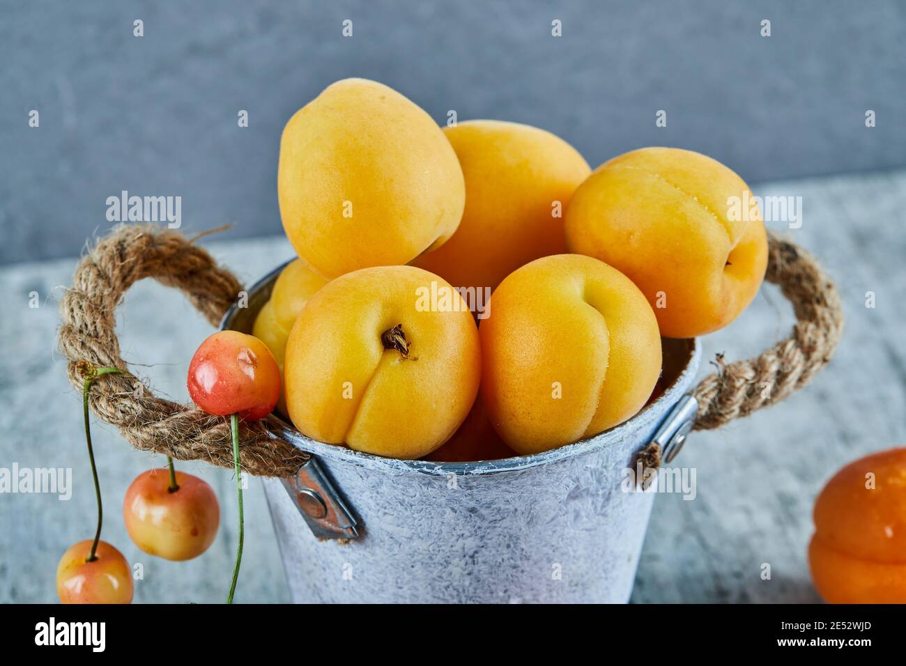 Delicious ripe apricots in iron bucket with cherries on marble
