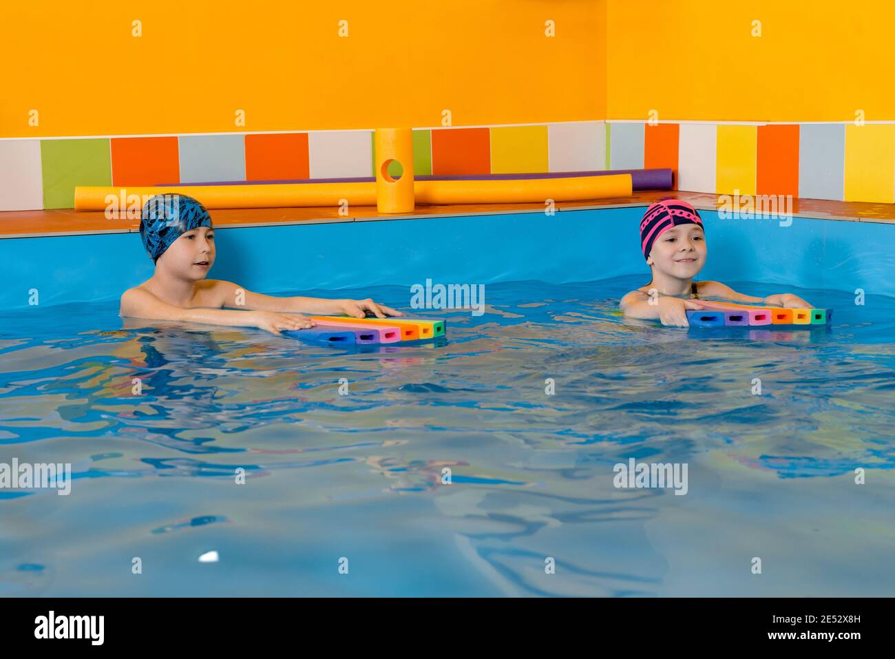 Boy and girl wearing swimsuit uses a foam pad to practice swimming in