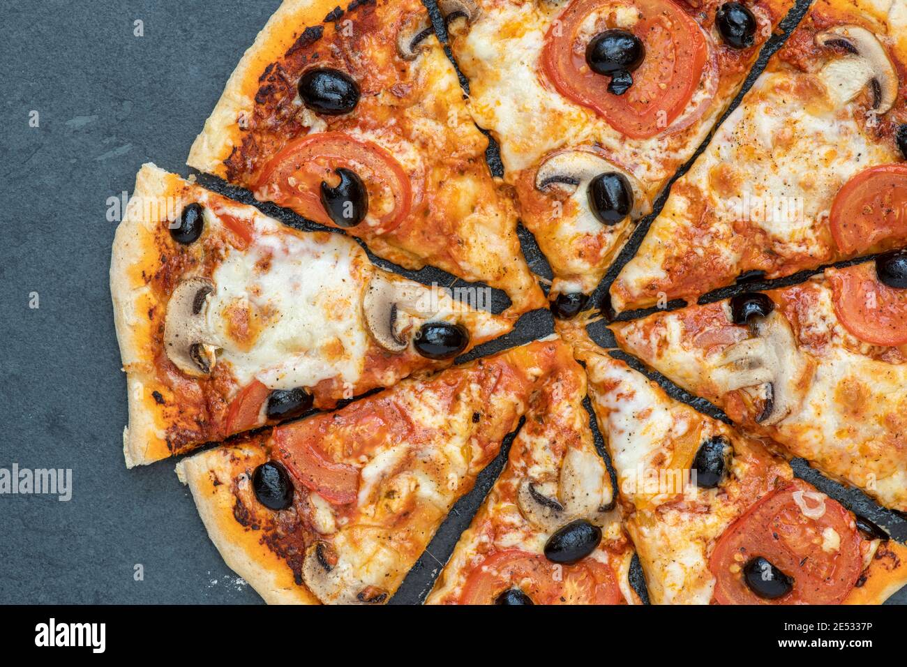 Homemade vegetarian tomato and mushroom pizza cut into slices on a slate background Stock Photo