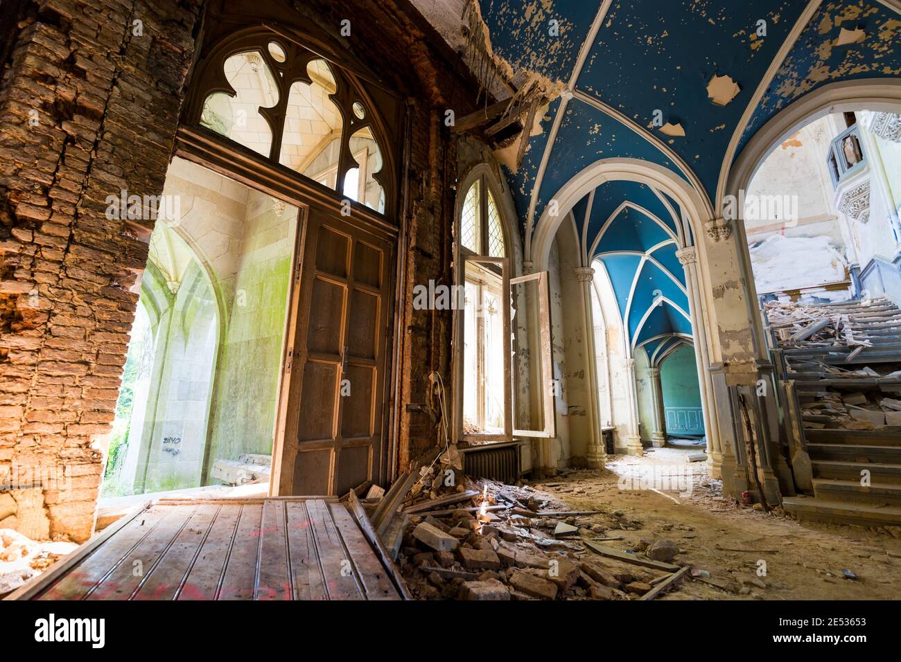 Wide angle shot of the interior of an old and abandoned baroque castle, with pointed arches and blue cross vaults Stock Photo