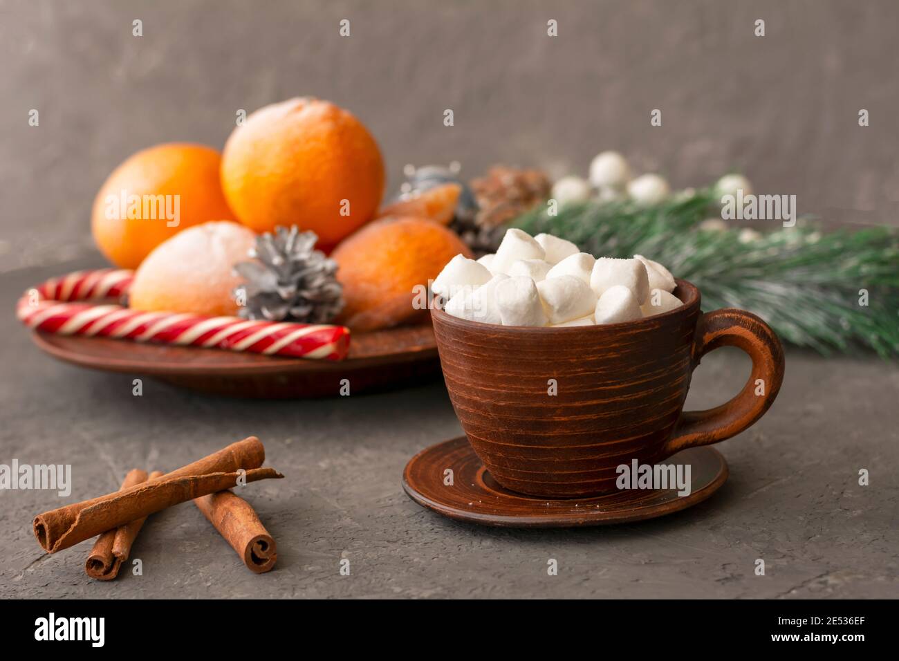 Coffee with marshmallows in brown clay cup. Tangerines and cinnamon in winter composition on concrete wall. Selective focus, blurred background. Stock Photo