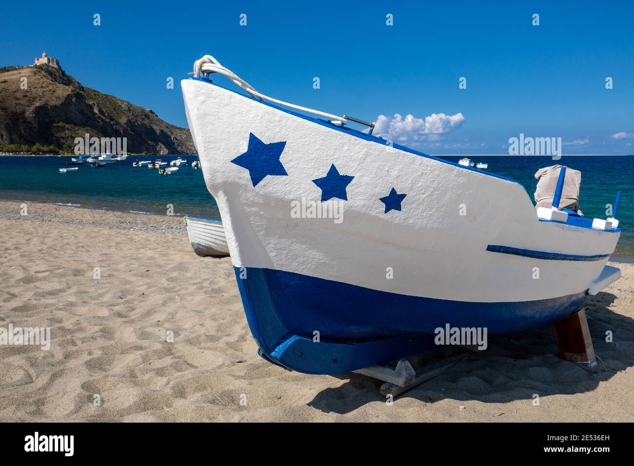 Close up of a white and blue fishing boat decorated with stars on its prow, lying ashore on a sandy beach in a sunny summer day Stock Photo