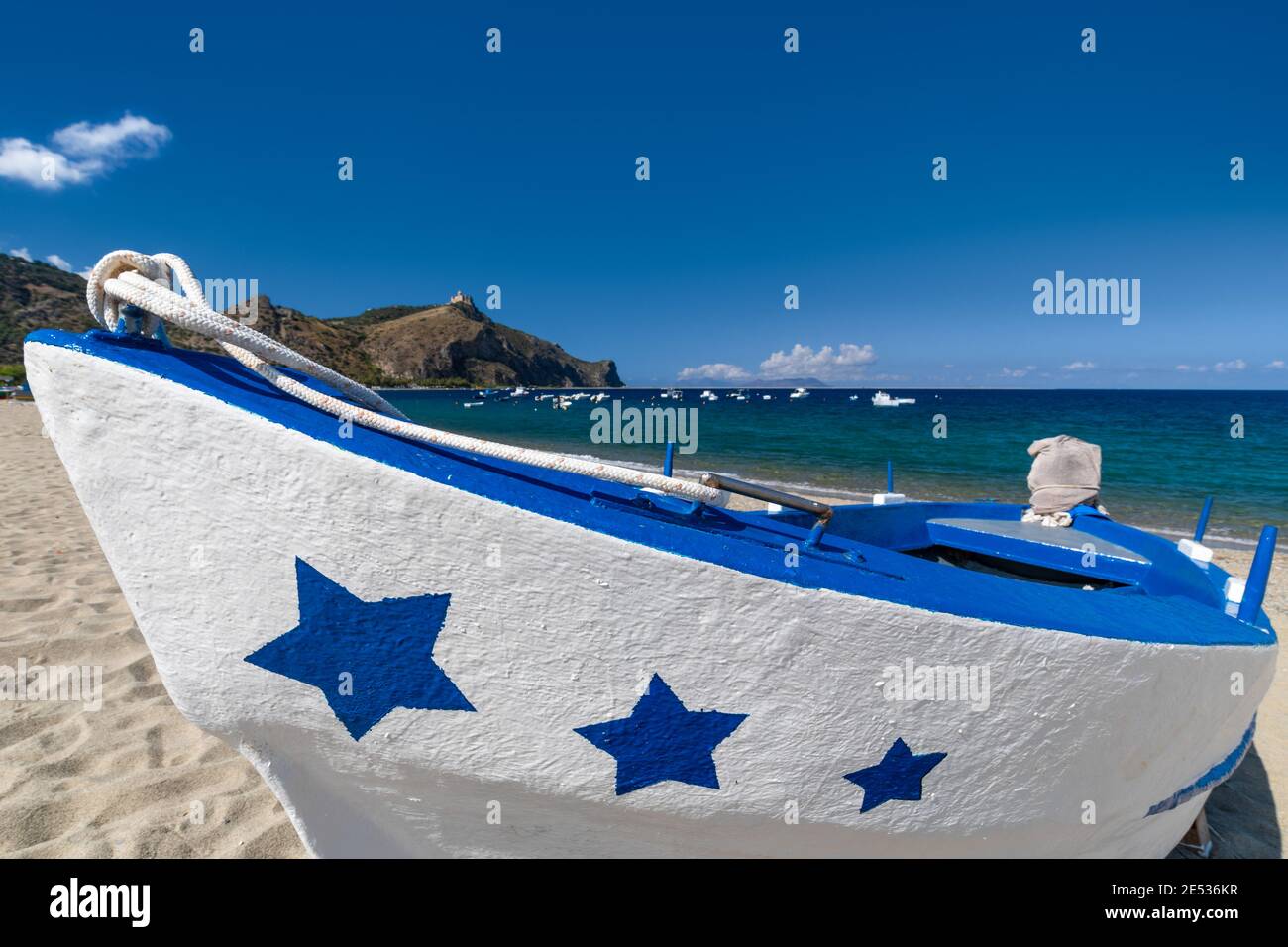 Close up of a white and blue fishing boat decorated with stars on its prow, lying ashore on a sandy beach in a sunny summer day Stock Photo