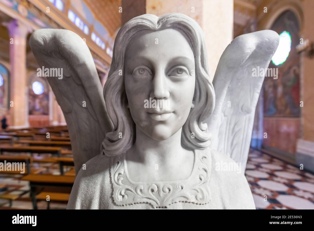 Close up of a white marble statue of a winged angel against the nave of a colorful church Stock Photo