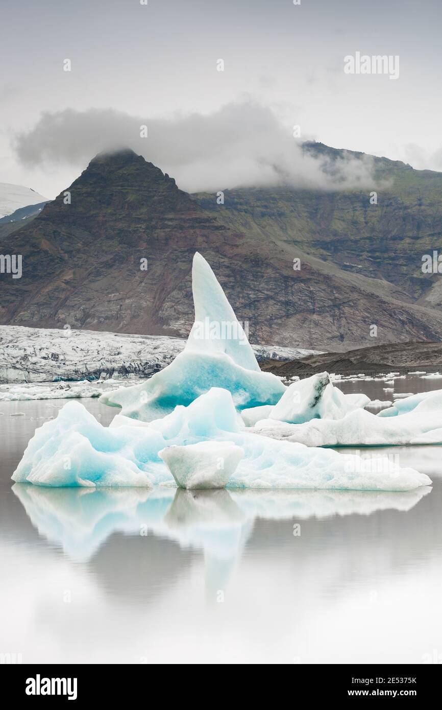 Close up of an iceberg floating in front of a glacier in the iconic Jokulsarlon lagoon in Iceland, under a cloudy sky Stock Photo