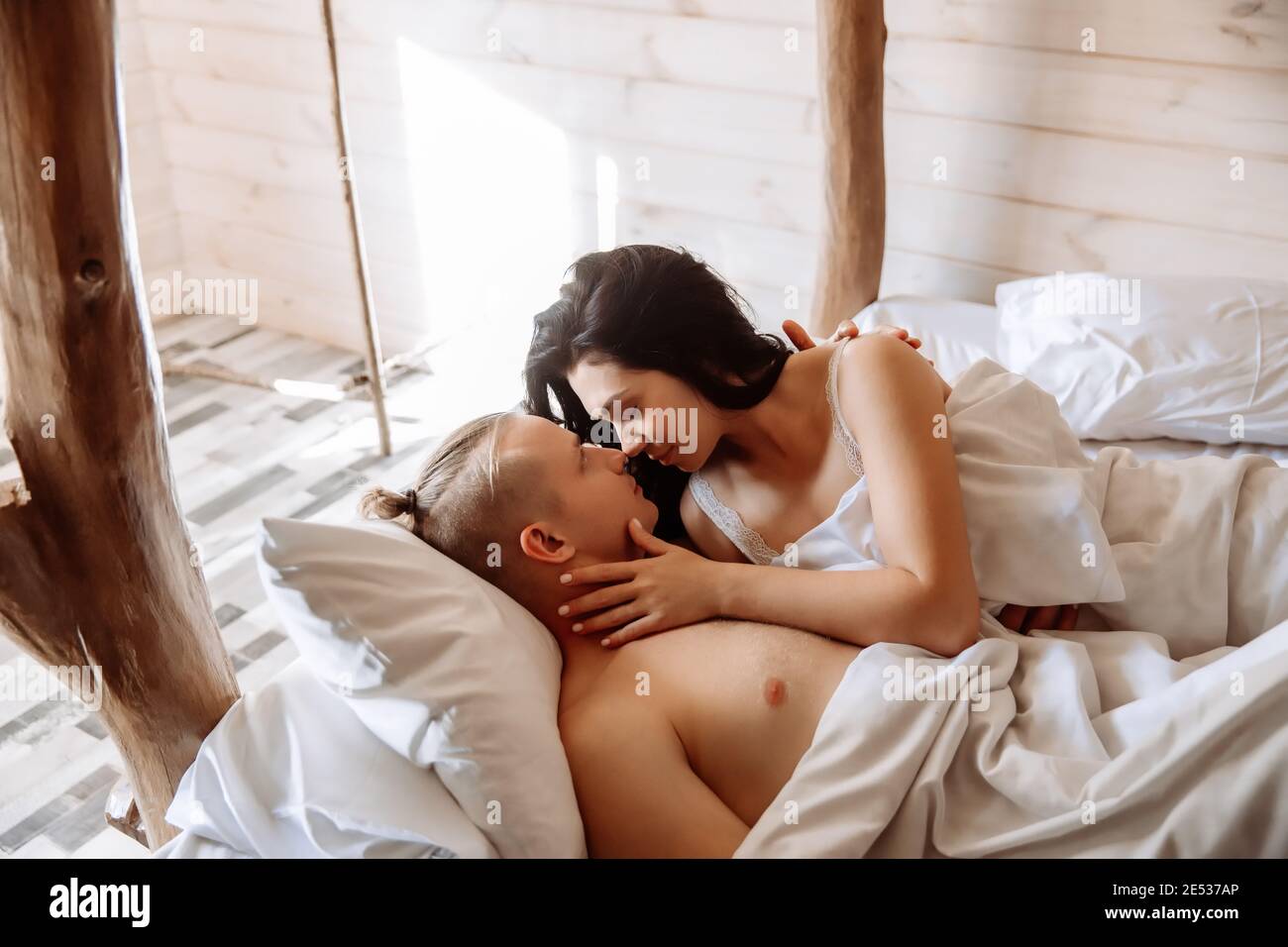 Young couple in love, man and woman, lie in bed under a white blanket. They look at each other with tenderness. Stock Photo
