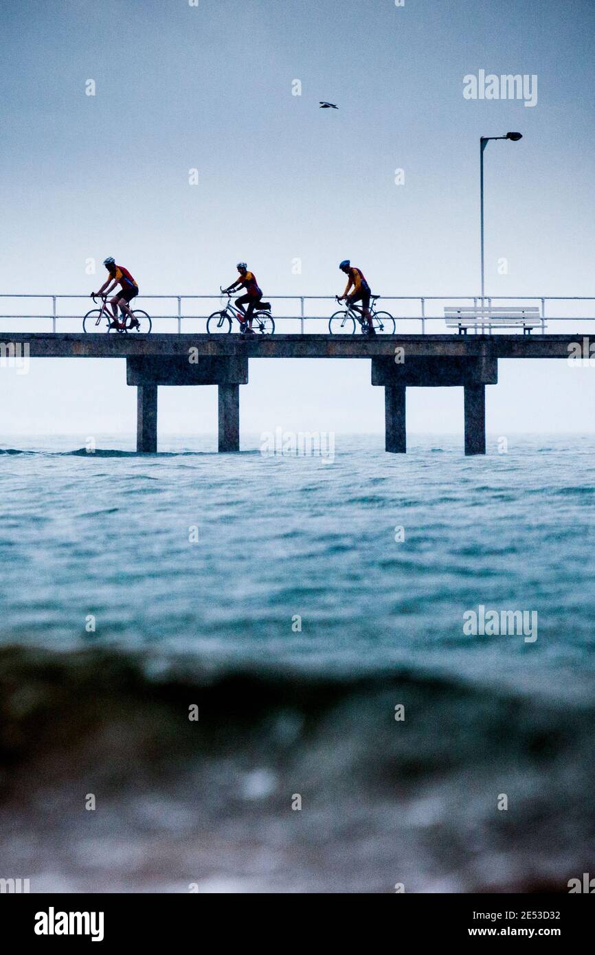 Touring cyclists in the rain on the pier at Cowes, Phillip Island. Stock Photo