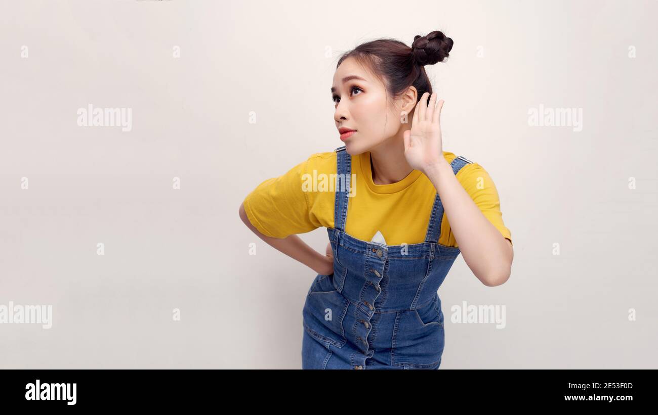 Eavesdropping Concept. Asian girl holding her hand near ear and listening carefully isolated over white wall, copyspace Stock Photo
