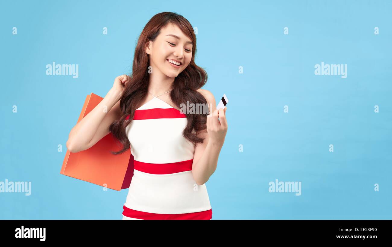 Trendy beautiful young Asian woman carrying colorful bags shopping online with mobile phone isolated on bluer background Stock Photo