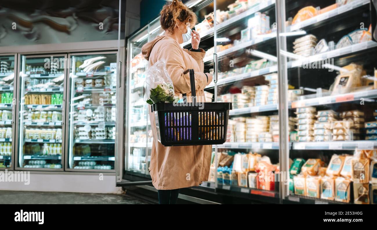 Female shopper with face mask in a supermarket. Female customer shopping grocery during pandemic. Stock Photo
