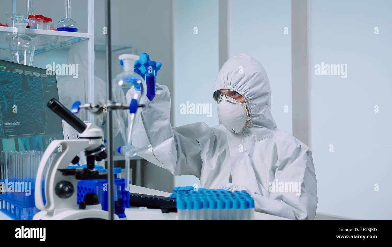 Medical scientist with coverall in laboratory room performs tests with ...