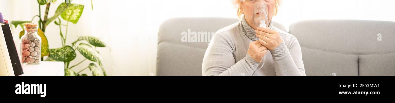 Elderly woman using asthma machine on light background Stock Photo