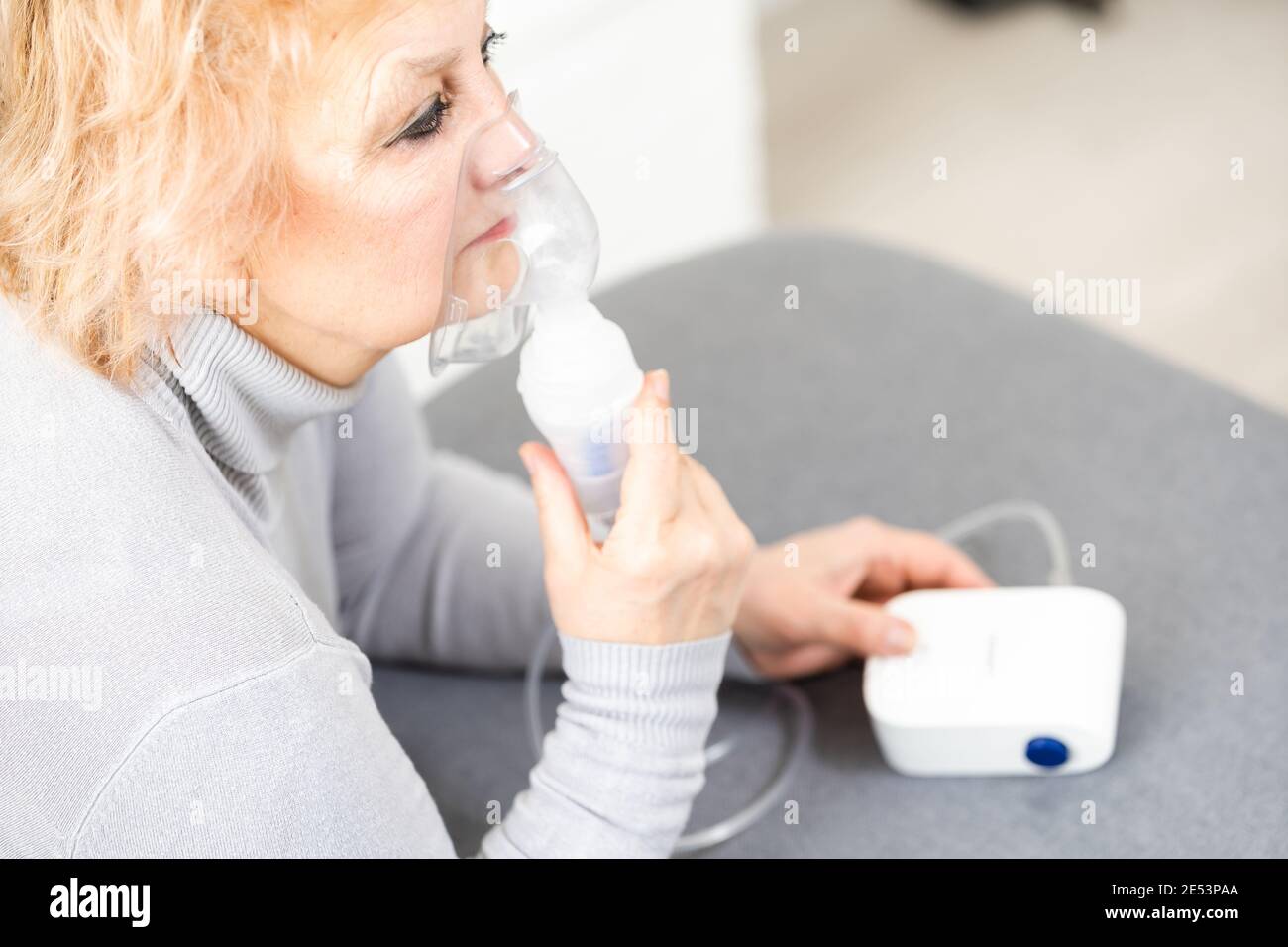 Elderly woman using asthma machine on light background Stock Photo