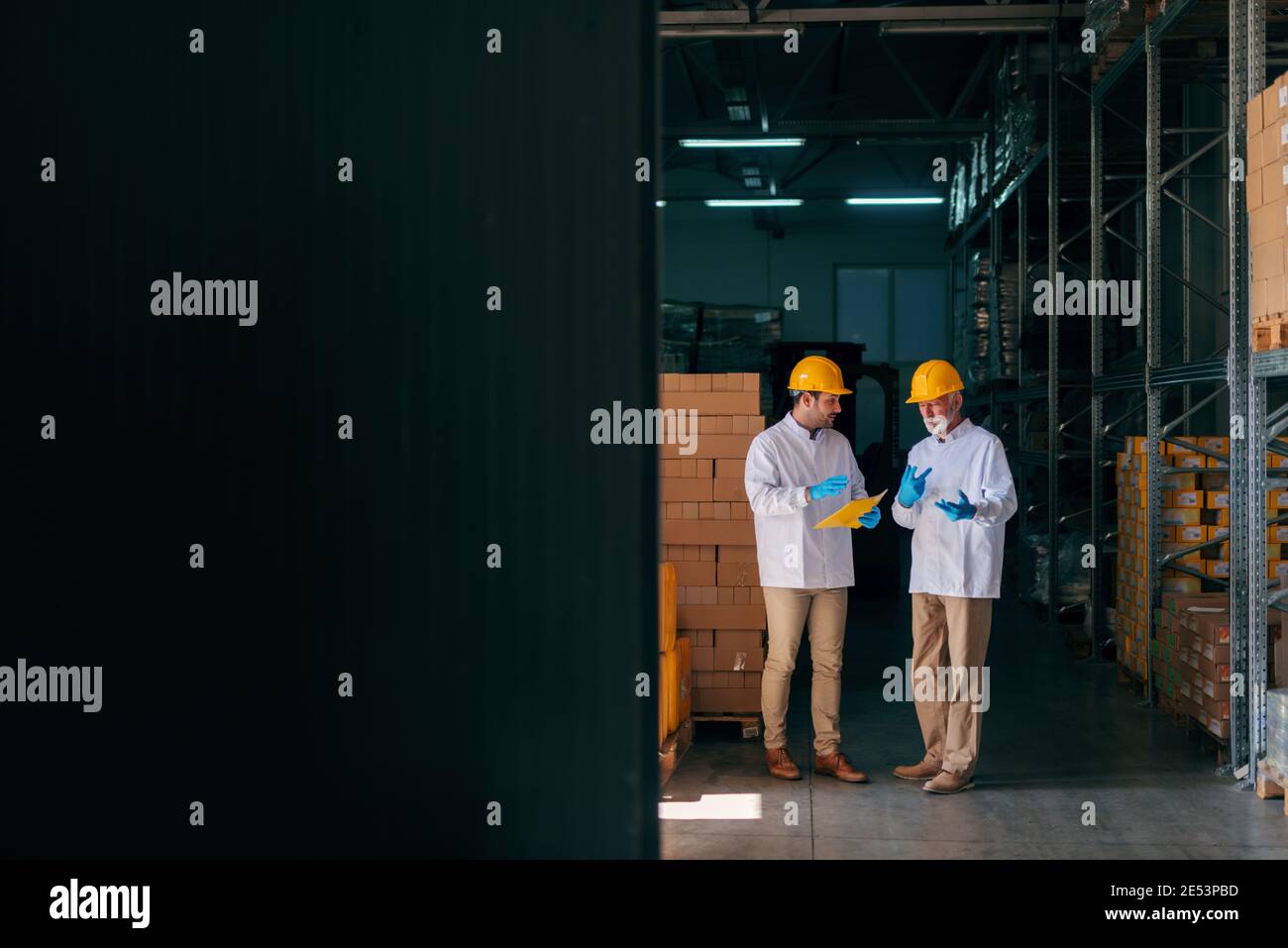 Two Caucasian workers discussing while younger worker holding documents. Warehouse interior. Stock Photo