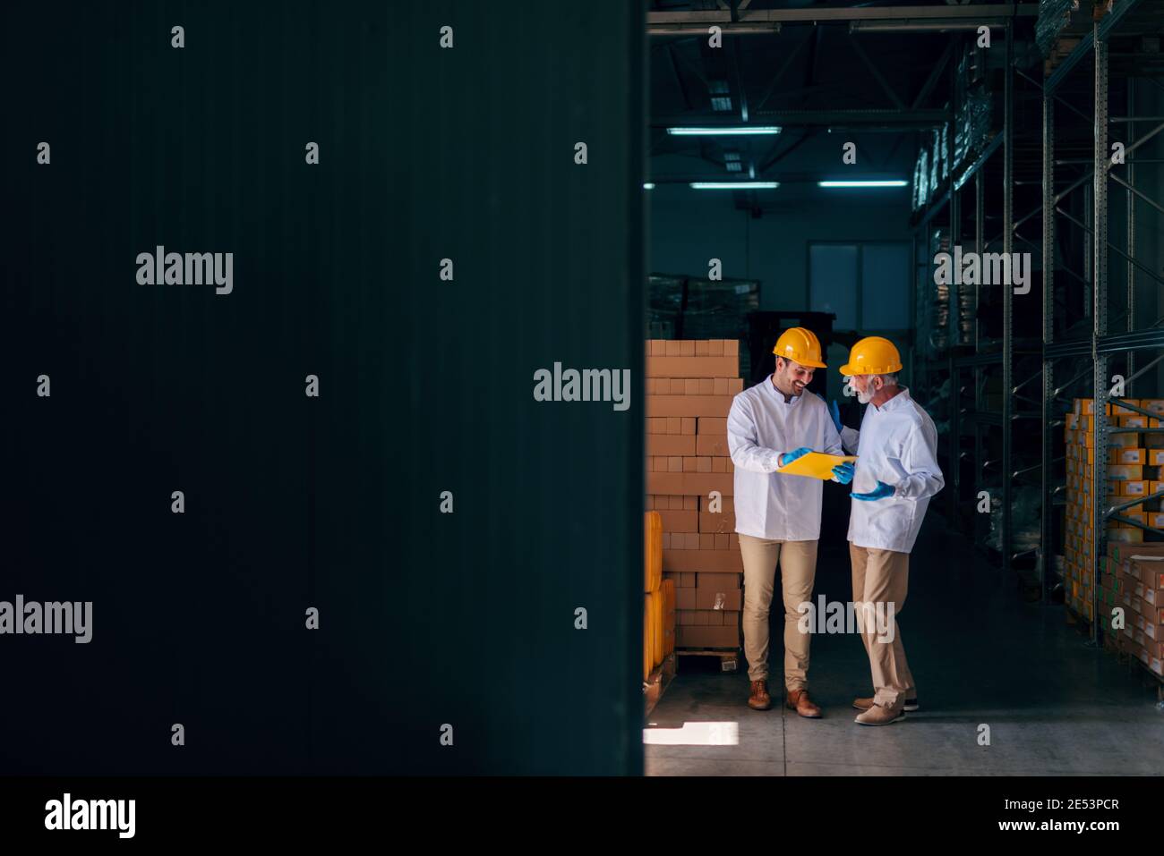 Two Caucasian workers discussing while younger worker holding documents. Warehouse interior. Stock Photo