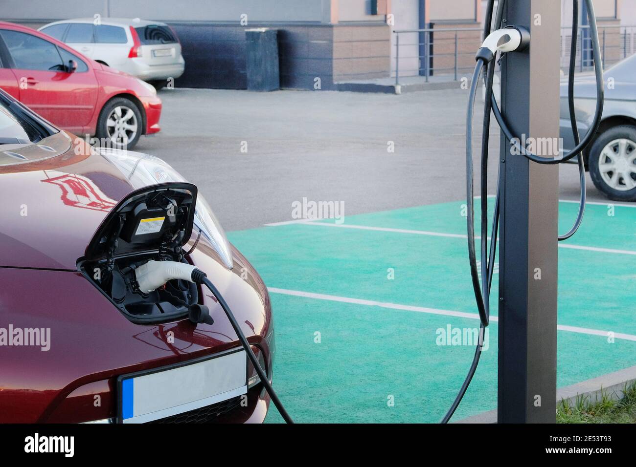 Red auto is charged on electric charging station in parking lot. Eco friendly transport concept. Loading energy. Modern alternative energy. Stock Photo