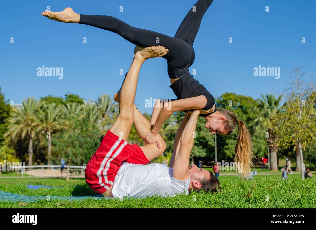 The Theme Of Acroyoga And Yoga Poses. A Pair Of Two Men And A Woman Stand  In The Position Of Asana. The Guy Holds The Girl Arched High Back On The  Outstretched