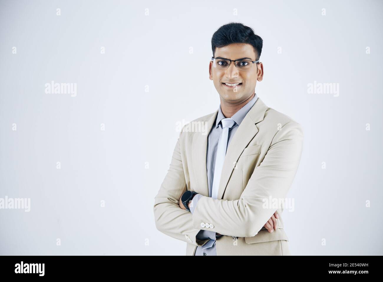 Studio portrait of smiling confident Indian businessman in suit folding arms and looking at camera Stock Photo