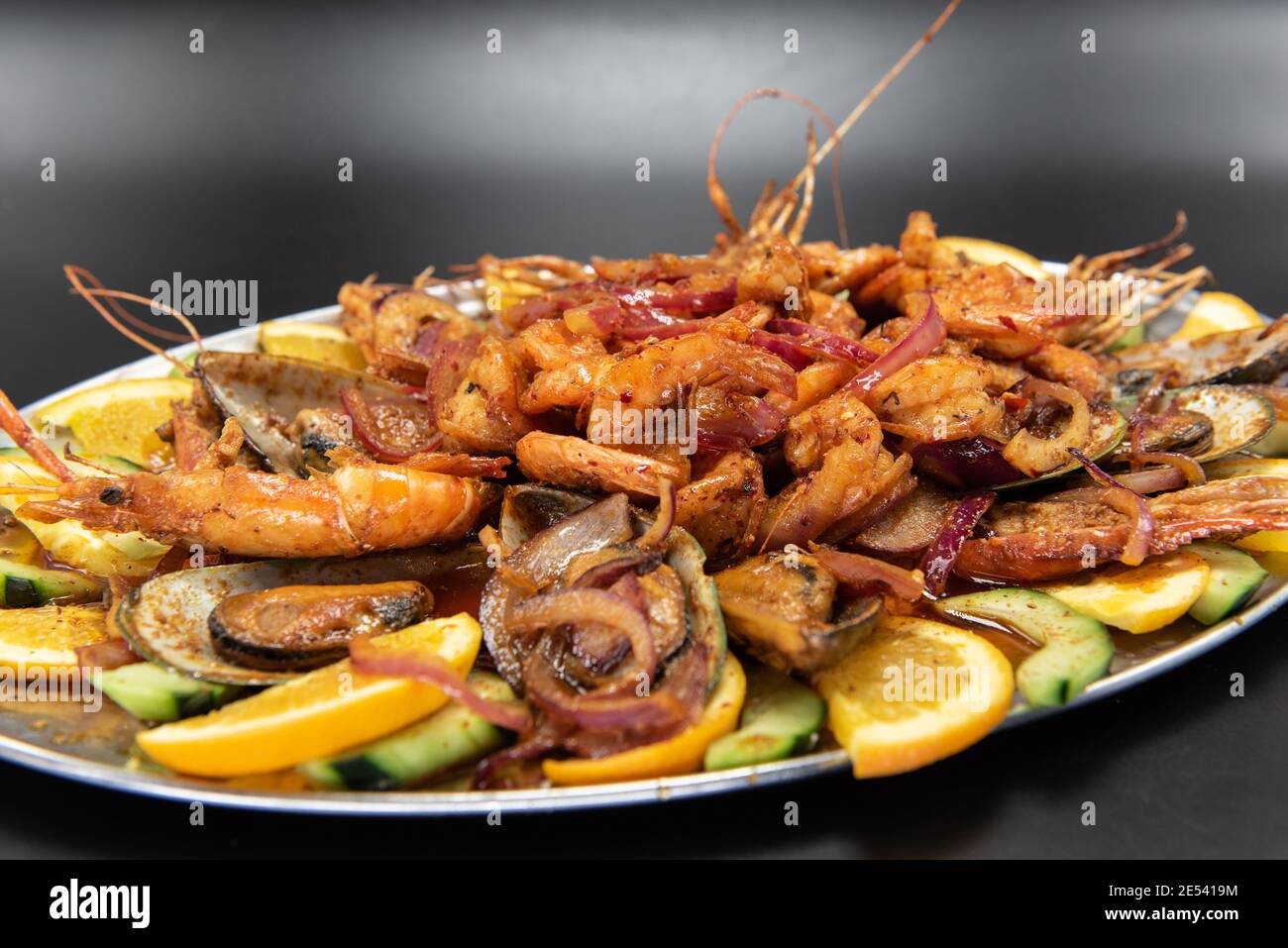 Large pile of spicy shrimp plate served over roasted vegetables and garnished with orange slices. Stock Photo